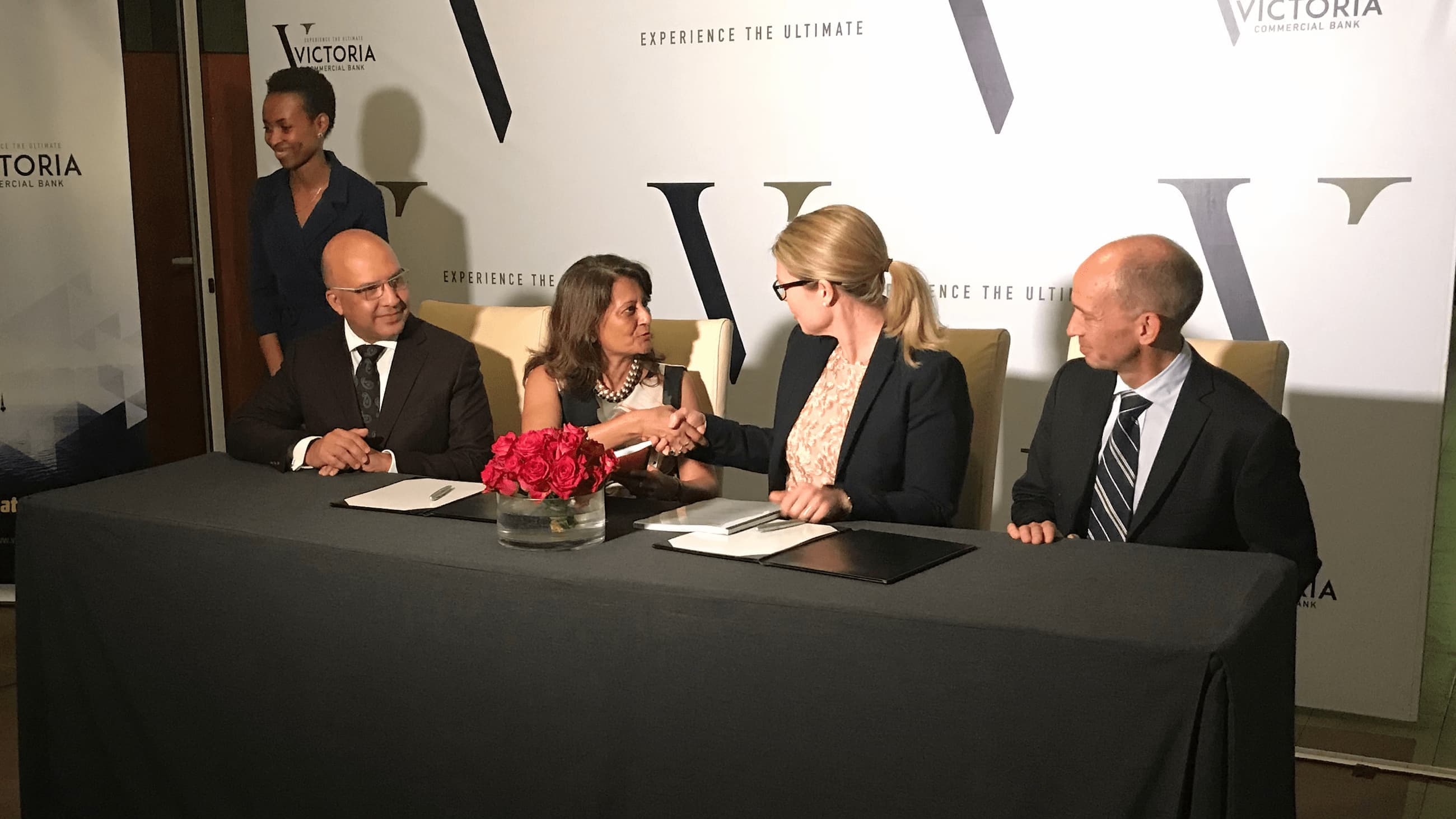 Two women and two men are sitting at a table. The women shake hands.
