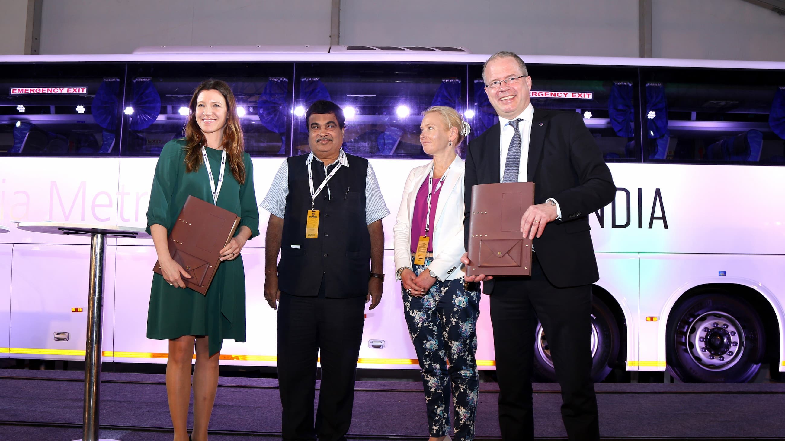 Four people standing on a podium in front of a bus