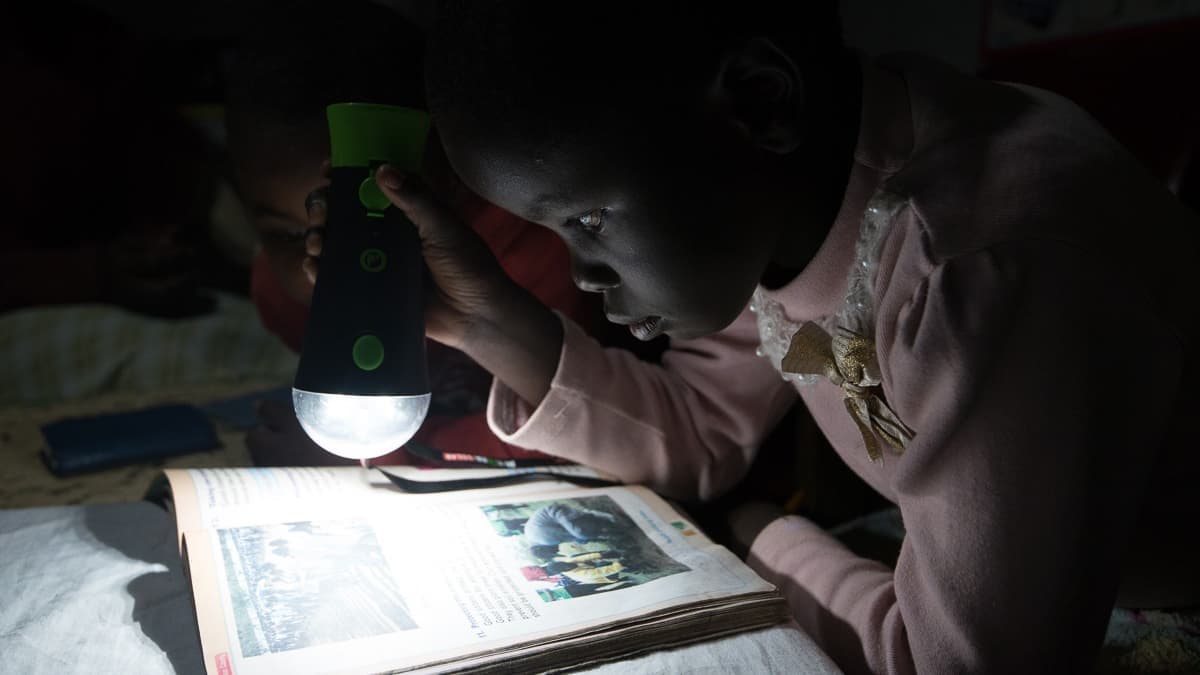 Ett barn i Kenya läser i ljuset från en uppladdningsbar lampa